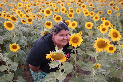 Portrait of smiling fat woman amidst sunflowers blooming on field