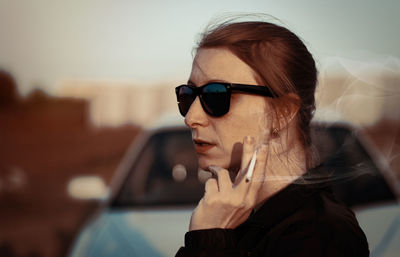 Young woman smoking cigarette while wearing sunglasses