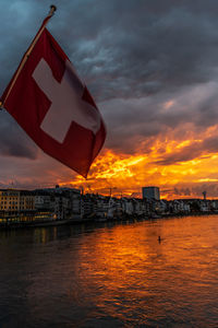 Scenic view of river by buildings against sky during sunset