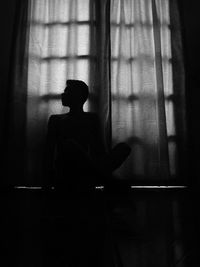 Silhouette woman looking at window in dark room