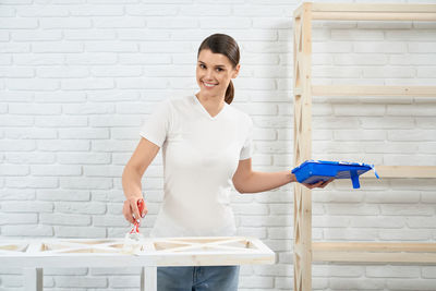 Portrait of a smiling young woman standing against wall