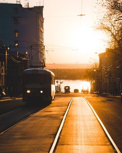 Illuminated railroad tracks in city against sky during sunset