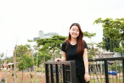 Portrait of smiling young woman standing against clear sky