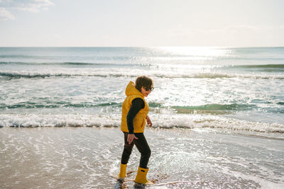 Rear view of woman standing at beach against sky