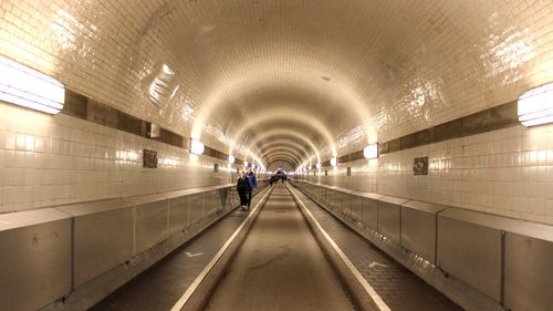 Rear view of man walking in illuminated tunnel