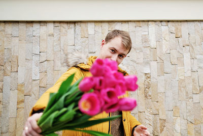 Blond man in a yellow winter jacket with a bouquet of tulips in hands