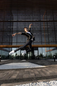 Young attractive dancer in casual cloth doing ballet jump on the urban