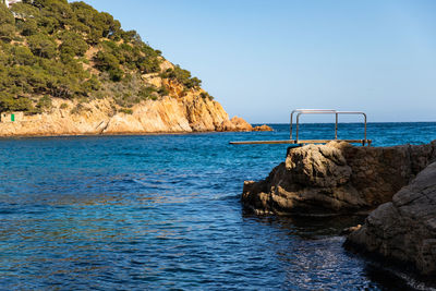 Rock formations by sea against clear blue sky