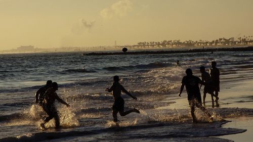 Silhouette people playing football in sea against sky