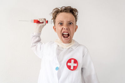 Portrait of boy holding syringe against white background