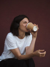 Pretty young woman with headphones listening to music and drinking coffee.