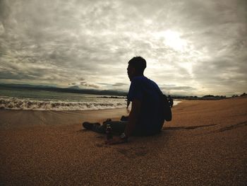 Rear view of man sitting on shore at beach against sky