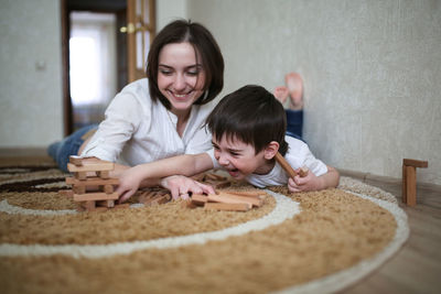 Beautiful brunette mom playing with kid boy on the floor in wooden designer, casual lifestyle 