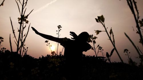 Silhouette woman standing on field against sky during sunset