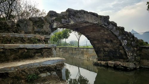 Old arch bridge over canal against sky