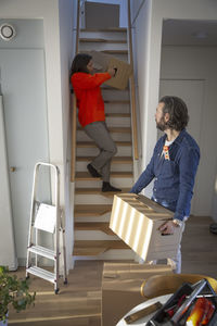 Mature woman and man carrying boxes on steps at new home