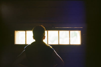 Rear view of silhouette man standing against window