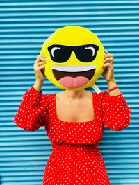 Woman covering face with anthropomorphic face cushion against shutter