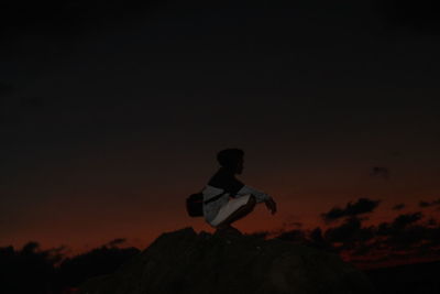 Silhouette man sitting on rock against sky during sunset