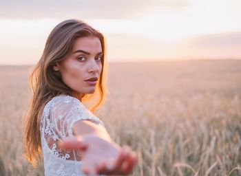 Portrait of beautiful young woman in farm against sky during sunset