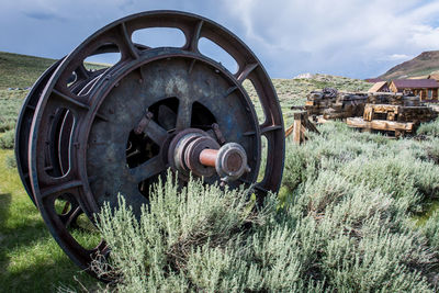 Close-up of old machinery on field against sky