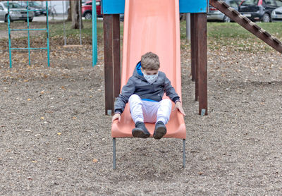 Small boy with protective face mask sliding on the playground.