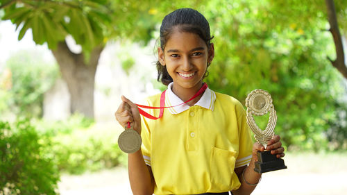 Portrait of a happy school girl wearing school uniform celebrating victory trophy in hand.