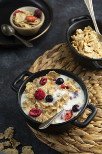 Breakfast with wholemeal corn flakes, berries in black bowls.