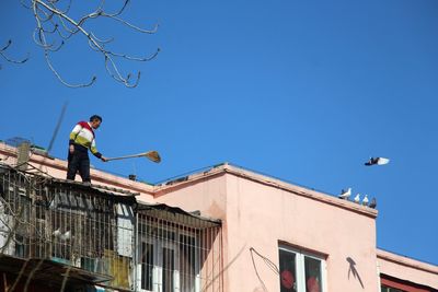 Low angle view of man working on building against clear blue sky