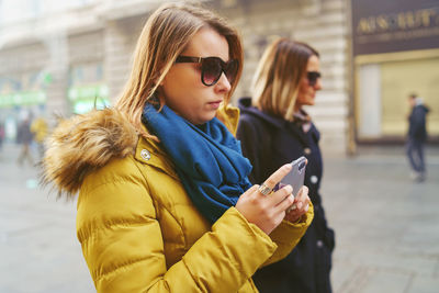 Young woman with friend using phone on street in city