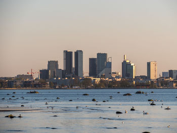 Sea by buildings against clear sky during sunset in city