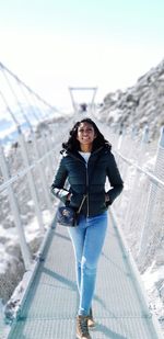 Portrait of smiling young woman standing on footbridge against mountains