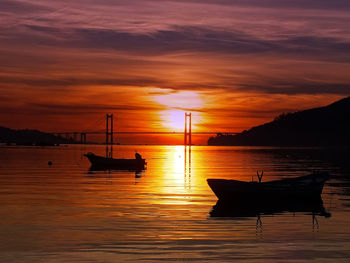 Silhouette boat moored on sea against orange sky