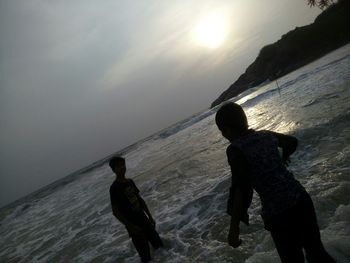Rear view of silhouette men standing at beach during sunset