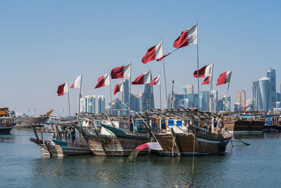 Sailboats with qatar flag in city by buildings against clear sky, doha, qatar 