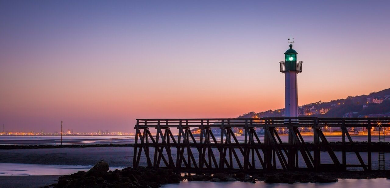 clear sky, sunset, copy space, guidance, built structure, sea, water, lighthouse, architecture, illuminated, orange color, railing, direction, bridge - man made structure, dusk, sky, connection, tranquility, building exterior, nature