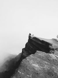 Man sitting on rock formations against clear sky