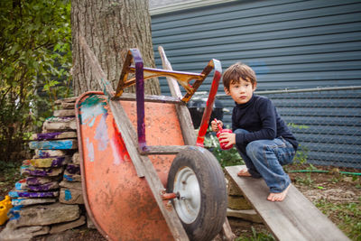 A small barefoot boy paints an old wheelbarrow with bright colors