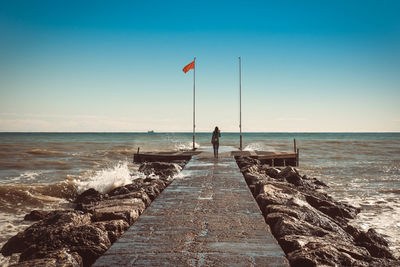 Rear view of woman walking on pier in sea against blue sky