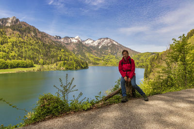 Full length of woman sitting at lakeshore against cloudy sky