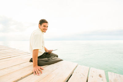 Full length of man sitting on chair at sea shore against sky