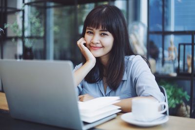 Portrait of smiling young woman using phone on table