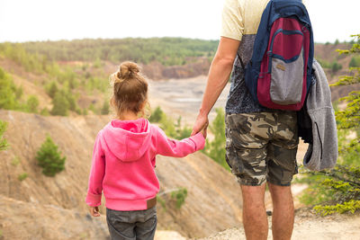 Daughter in a pink hoodie holding dad's hand, standing on top of a mountain with 