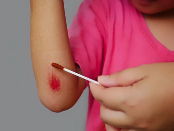 Midsection of boy with wounded hand standing against gray background