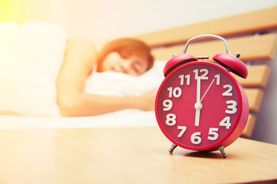 Close-up of alarm clock on table with woman sleeping on bed at home