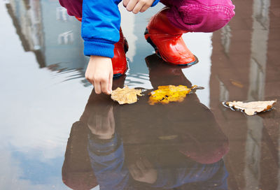 Low section of girl wearing rubber boots while picking leaf from puddle