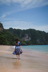Rear view of woman at beach against sky