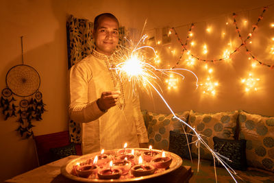 Young man in traditional dress holding the fireworks in hand with ferry lights background