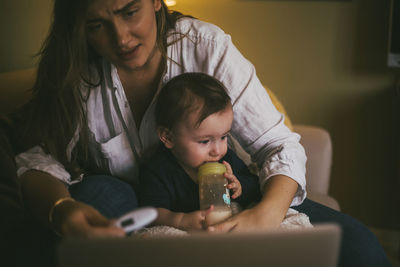 Midsection of mother and daughter sitting in bedroom