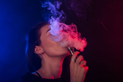 Close-up of woman smoking cigarette against black background